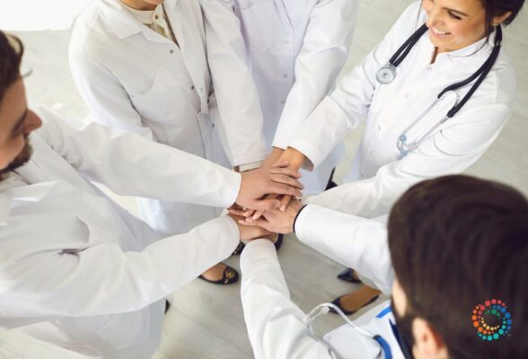 View looking down on five physicians with hands reaching into center of a circle symbolizing consensus